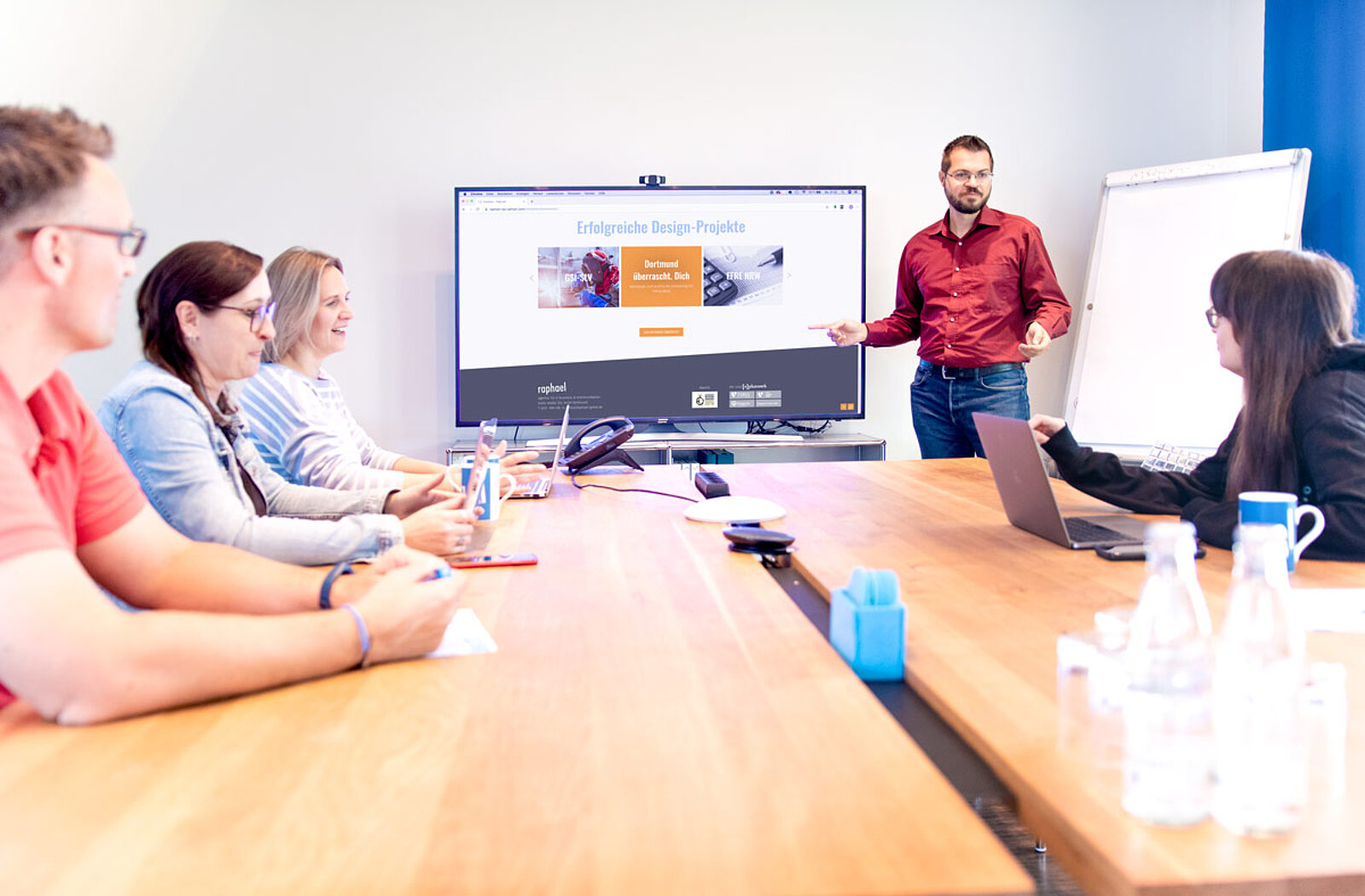 Menschen sitzen zusammen an einem Tisch während eine Person an der Flipchart präsentiert